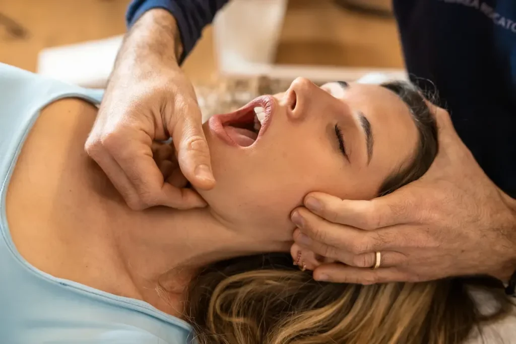 Woman receiving jaw alignment therapy from practitioner.